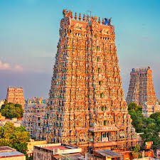 A tall Dravidian-style Meenakshi Amman Temple gopuram adorned with thousands of intricate, colorful sculptures against a blue sky.