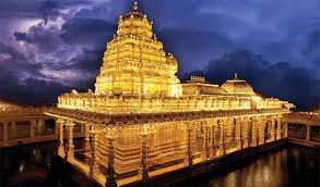 "The Sripuram Golden Temple in Vellore illuminated at night, with its brilliant gold architecture reflecting in the surrounding water under a dark, cloudy sky."